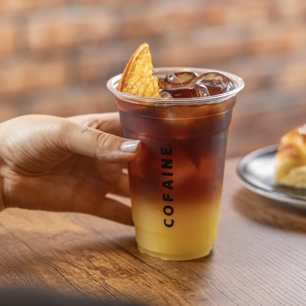 Café con naranja de Cofaine, servido para llevar sobre la mesa de madera